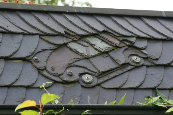 Schieferornament Ein kunstvolles Dachornament in Form eines Autos aus metallischen Schindeln.