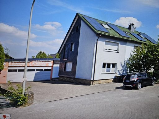 Fassaden Zweifamilienhaus mit Solarpanelen, Garagen und Parkplatz in ruhiger Umgebung.