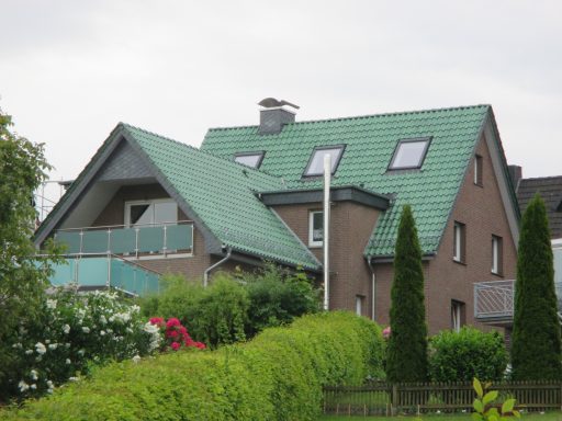 Ziegeldach Haus mit grünem Satteldach, Balkon und angrenzendem Garten mit Sträuchern und Blumen.