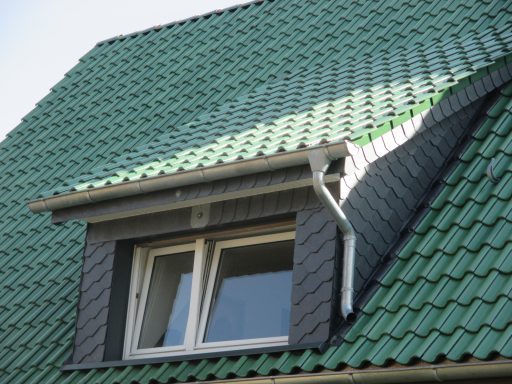 Schleppgaube Dachfenster in einem grünen Dach mit einem grauen Rollo.