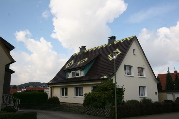 bunte Dächeindeckung Ein Haus mit einem schrägen Dach und grüner Fassadenverzierung unter einem blauen Himmel.