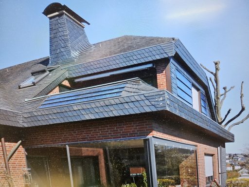 Schieferdach Moderne Hausansicht mit Steildach und großen Fenstern, umgeben von Gartenanlagen.