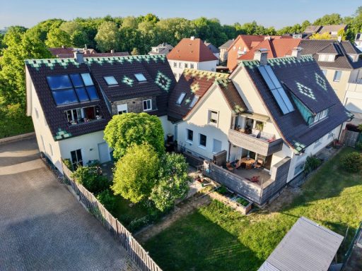 Ziegeldach Mehrfamilienhaus mit begrüntem Dach, Terrassen und Solarpanelen, umgeben von Bäumen.
