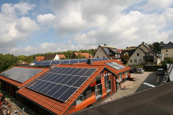 PV-Anlage Lagerhalle Dach mit Solarpanelen auf neuem Gebäude, umgeben von Wohnhäusern und einem Parkplatz.