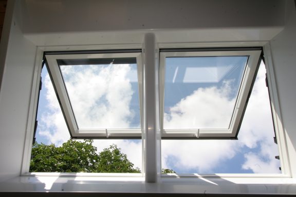 Dachfenster Offene Fenster zeigen einen blauen Himmel mit Wolken und Bäume im Hintergrund.